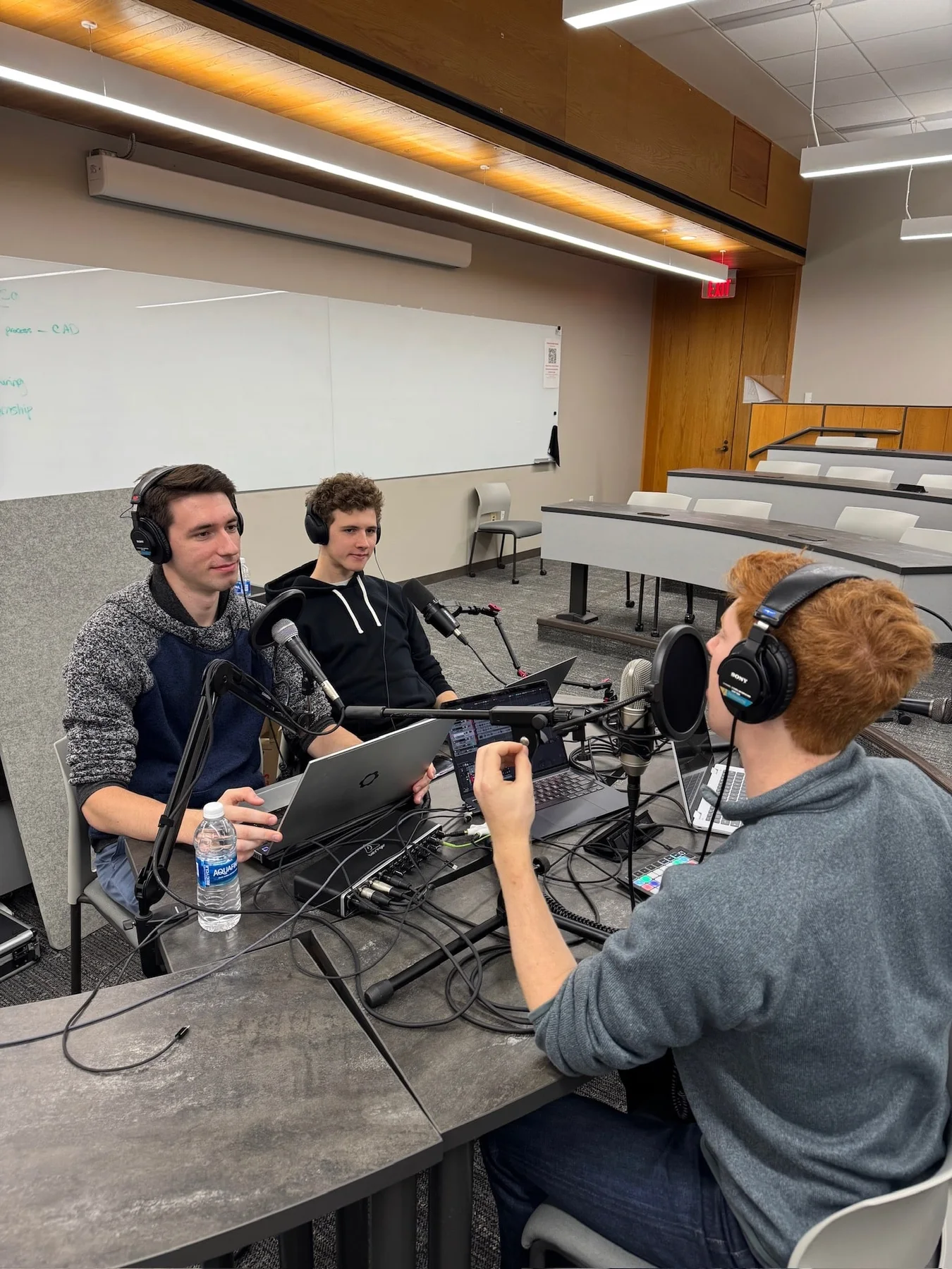 Three Beyond ME co-hosts recording around microphones and a laptop