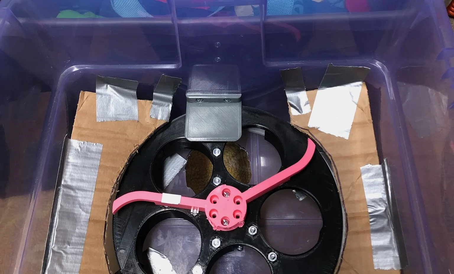 The gray TPU flap screwed to the side of the plastic container, sitting above the exit hole